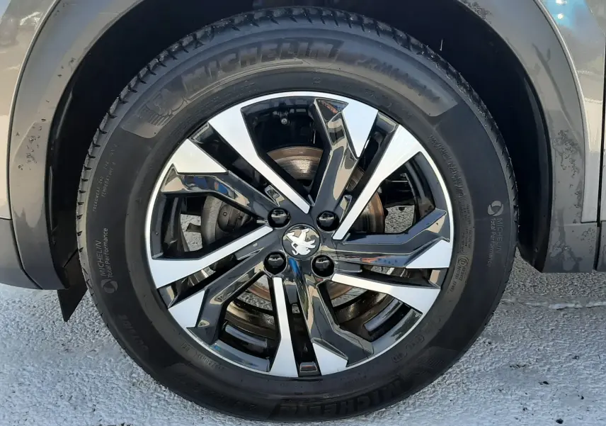 Gros plan sur la roue avant droite d'un Peugeot 2008 gris Artense avec jante alliage bicolore et pneu Michelin.
