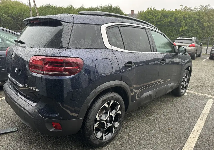 Vue 3/4 arrière droite d'un Citroën C5 Aircross Bleu Eclipse avec jantes alliage et toit ouvrant sous la pluie.