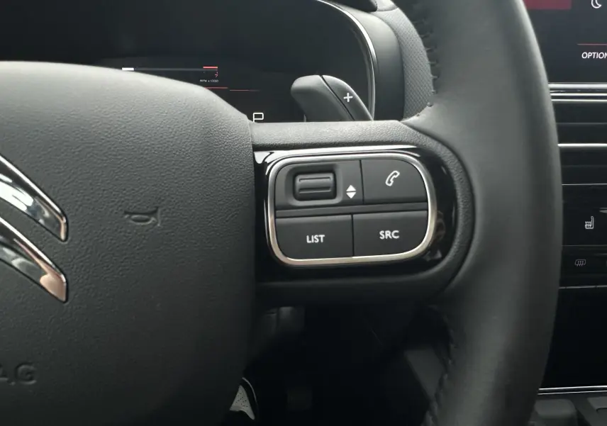 Gros plan sur le volant en cuir noir du Citroën C5 Aircross 2025, avec commandes intégrées côté droit.
