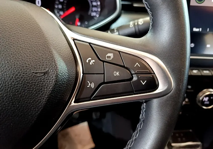 Gros plan sur le volant cuir synthétique noir de la Renault Clio Business TCe 100, avec commandes multifonctions visibles.