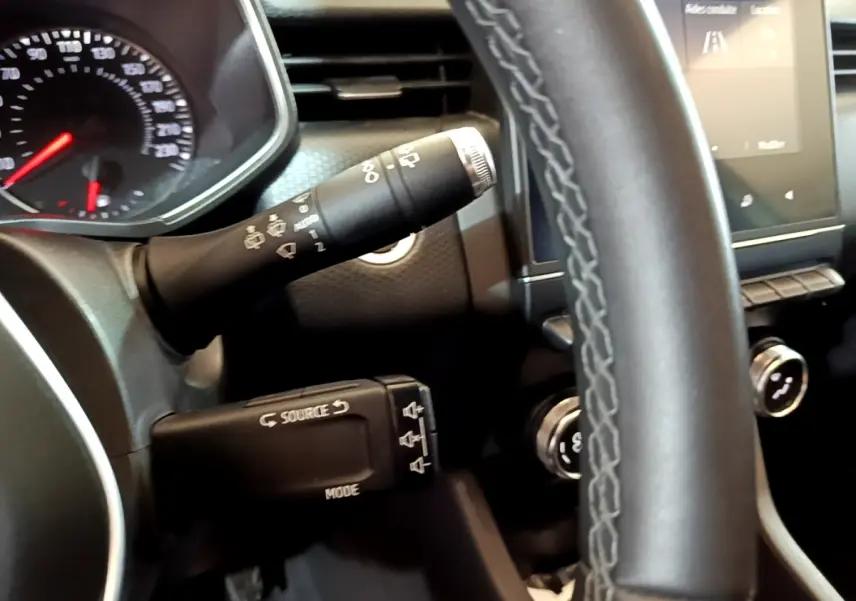 Gros plan sur le volant cuir synthétique et les commandes multifonctions de la Renault Clio Business TCe 100 blanche, tableau de bord visible.