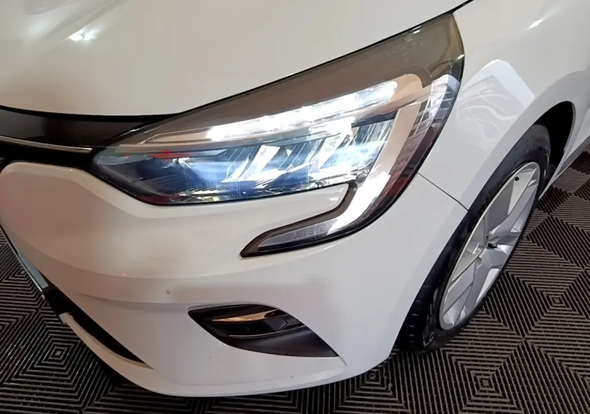 Gros plan sur l'avant droit blanc d'une Renault Clio 2020, mettant en valeur son phare LED et la jante alliage.