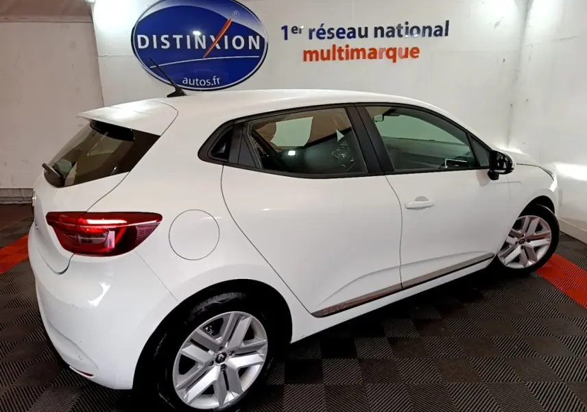 Vue 3/4 arrière droite d'une Renault Clio Business TCe 100 blanche, avec jantes alliage et feux arrière LED allumés.