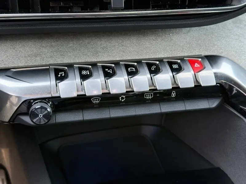 Gros plan sur la rangée de boutons métalliques du tableau de bord du Peugeot 3008 2024, avec bouton d'alerte rouge visible.