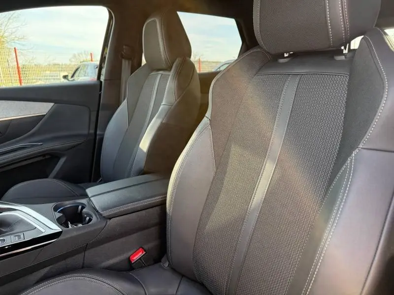 Gros plan sur les sièges avant en tissu noir du Peugeot 3008 2024, avec console centrale et accoudoir visibles.