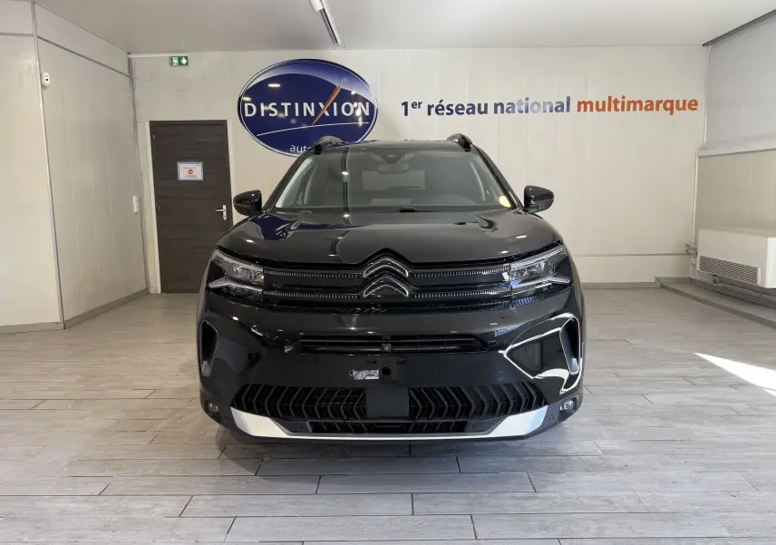 Vue frontale d'un Citroën C5 Aircross noir brillant avec calandre distinctive et éclairage LED dans un showroom.