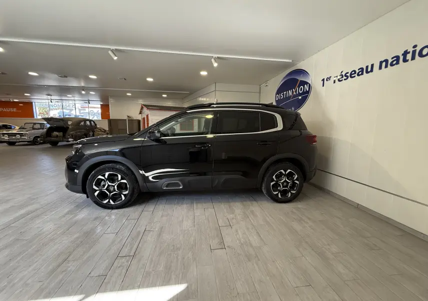 Vue de profil côté gauche d'un Citroën C5 Aircross gris Artense métallisé en showroom, avec jantes noires et détails chromés.