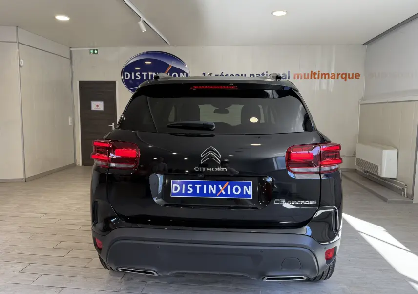 Vue arrière d'un Citroën C5 Aircross noir brillant en showroom, avec feux arrière allumés et logo Distinxion visible.