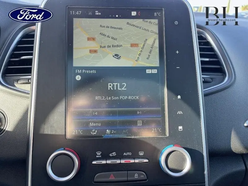 Gros plan sur l'écran tactile central du tableau de bord du Renault Scénic blanc nacré, affichant la navigation et la radio RTL2.