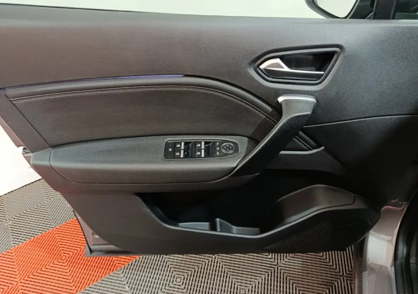 Vue intérieure côté gauche de la porte avant d’un Renault Captur gris foncé, avec commandes des vitres et poignée noire.