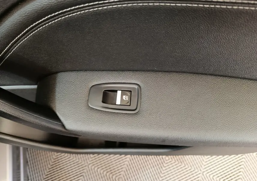 Gros plan sur le bouton de verrouillage centralisé sur la porte intérieure en cuir noir du Renault Captur gris foncé.