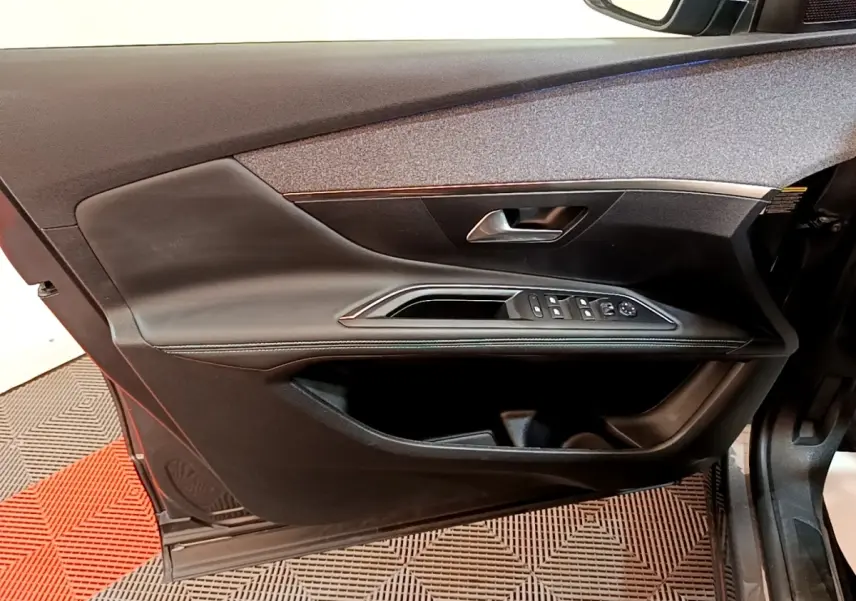 Vue intérieure côté gauche de la porte avant d’un Peugeot 3008 gris foncé avec commandes de vitres et poignée intégrée.