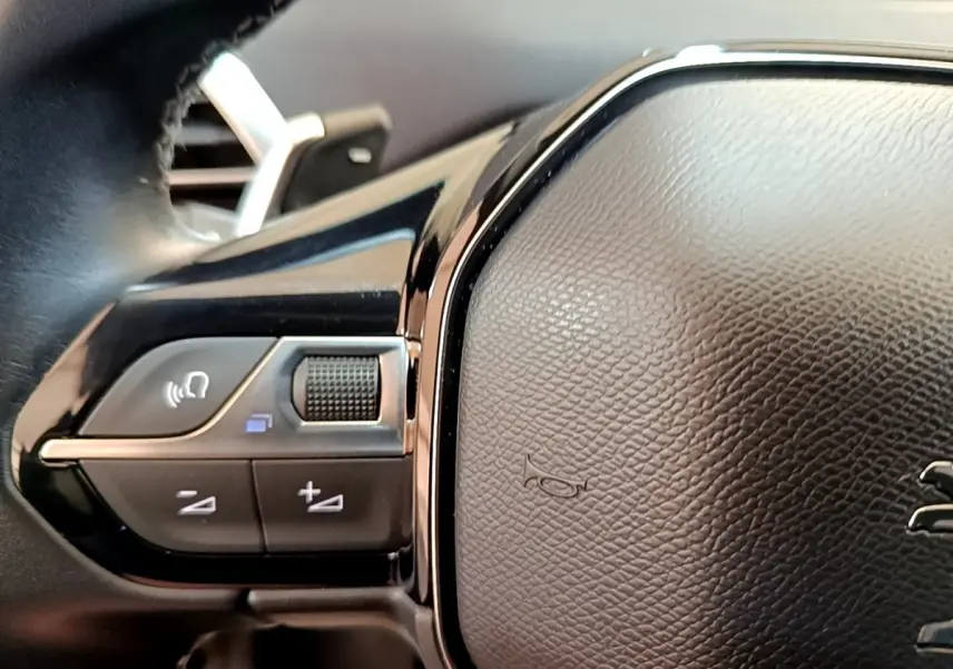 Gros plan sur les commandes gauche du volant cuir noir du Peugeot 3008 gris foncé hybride rechargeable 2022.