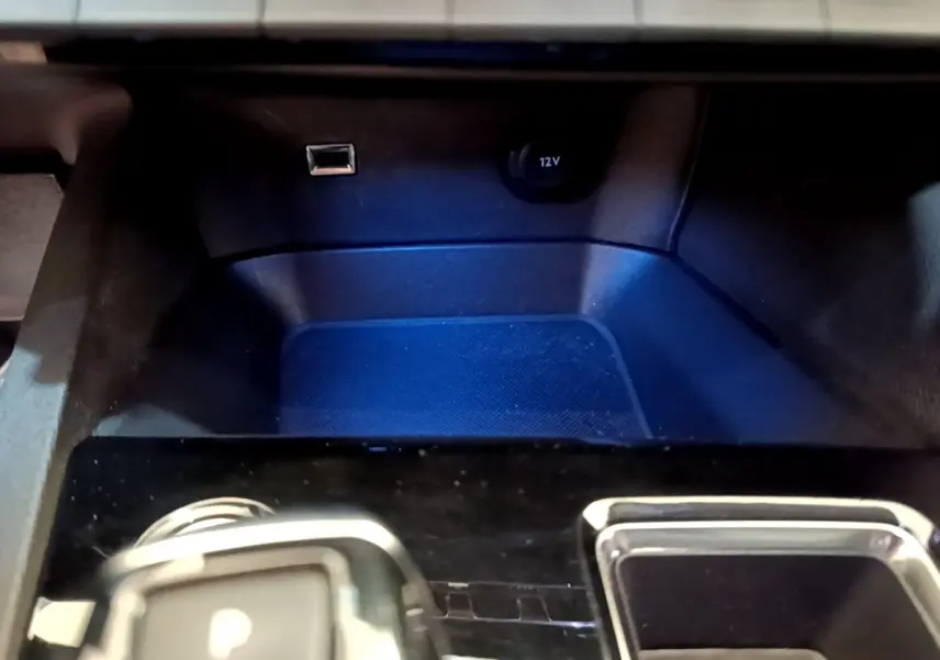 Gros plan sur la console centrale noire du Peugeot 3008 gris foncé, avec prise 12V et port USB visibles.