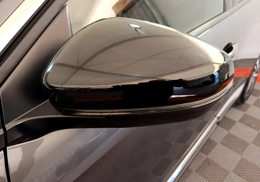 Rétroviseur droit noir brillant du Peugeot 3008 gris foncé, vue rapprochée avec reflet du plafond.
