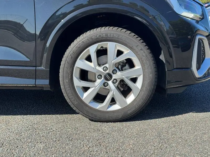 Gros plan sur la roue avant gauche de l'Audi Q2 35 TFSI S line 2023 en Noir Mythic métallisé, avec jante alliage et pneu Dunlop.