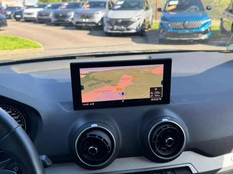Vue intérieure du tableau de bord de l'Audi Q2 35 TFSI S line 2023 avec écran GPS et aérateurs ronds noirs.