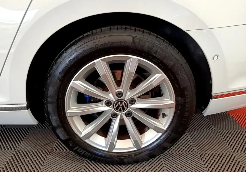 Gros plan sur la roue arrière droite d'une Volkswagen Passat blanche avec jante alliage et logo VW central.