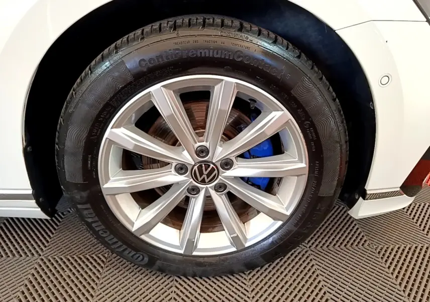 Gros plan sur la roue avant droite d’une Volkswagen Passat blanche avec jante alliage et étrier de frein bleu visible.