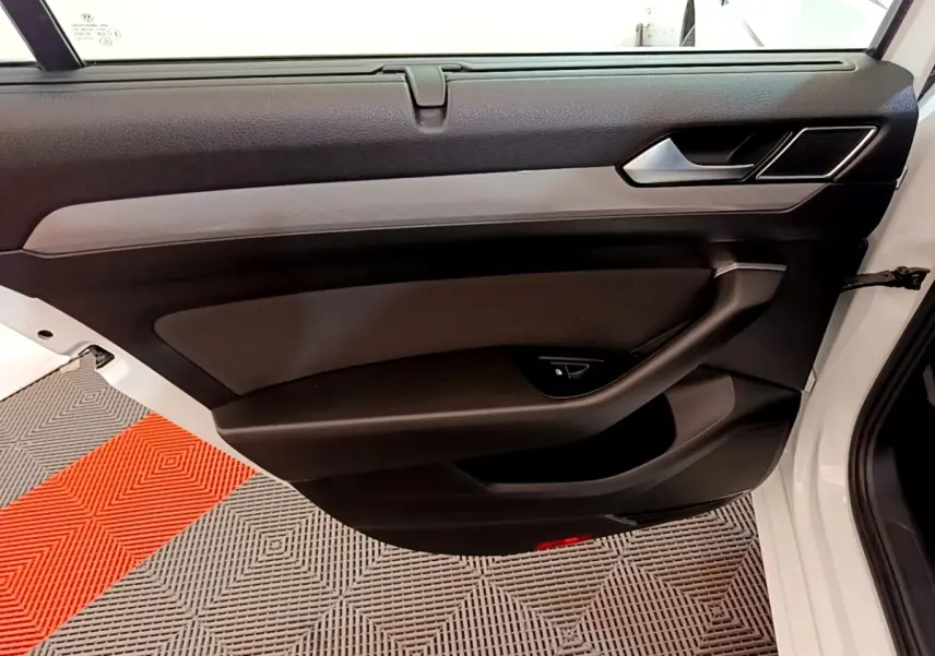 Vue intérieure de la porte avant droite noire et grise d'une Volkswagen Passat blanche, avec poignée et commande fenêtre.