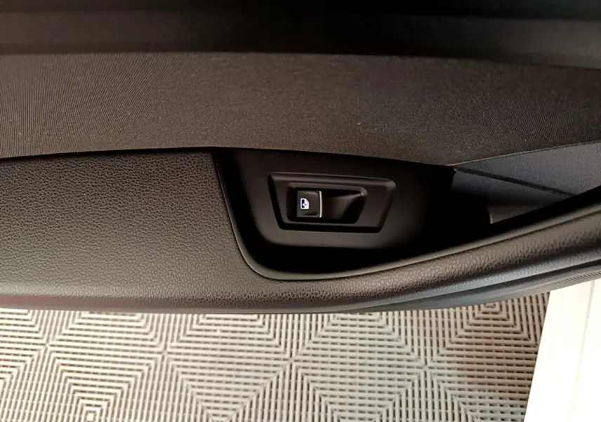 Détail du bouton d'ouverture électrique du coffre sur la porte intérieure d'une Volkswagen Passat blanche hybride rechargeable.