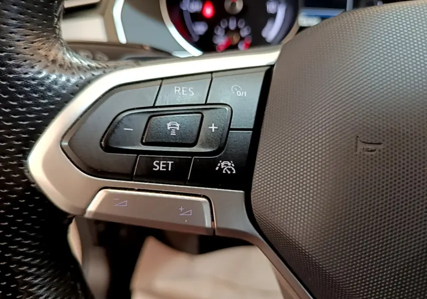 Gros plan sur les commandes de régulateur de vitesse au volant noir de la Volkswagen Passat hybride blanche.