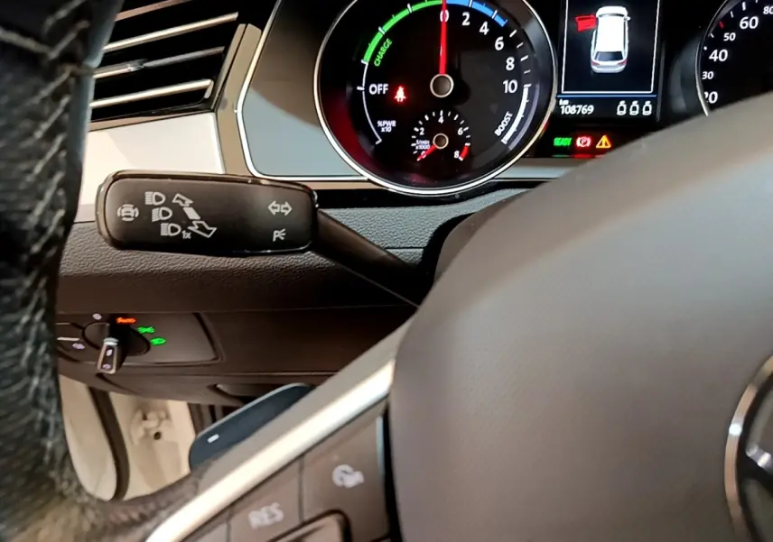 Vue rapprochée du tableau de bord et volant de la Volkswagen Passat hybride blanche, avec affichage digital et commandes au volant.