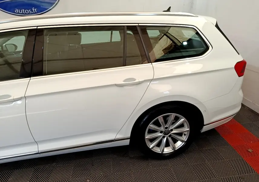 Vue côté droit arrière d'une Volkswagen Passat blanche break avec jante alliage et vitres teintées.