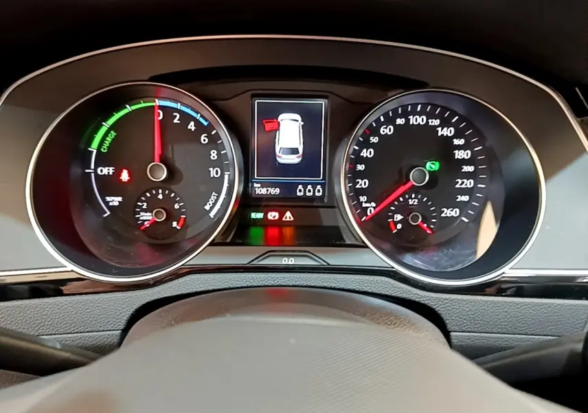 Vue rapprochée du tableau de bord digital de la Volkswagen Passat hybride blanche, affichant les compteurs et alertes.