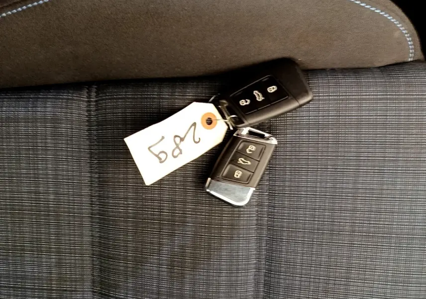 Clés de voiture Volkswagen Passat hybride posées sur un siège tissu gris à surpiqûres blanches.