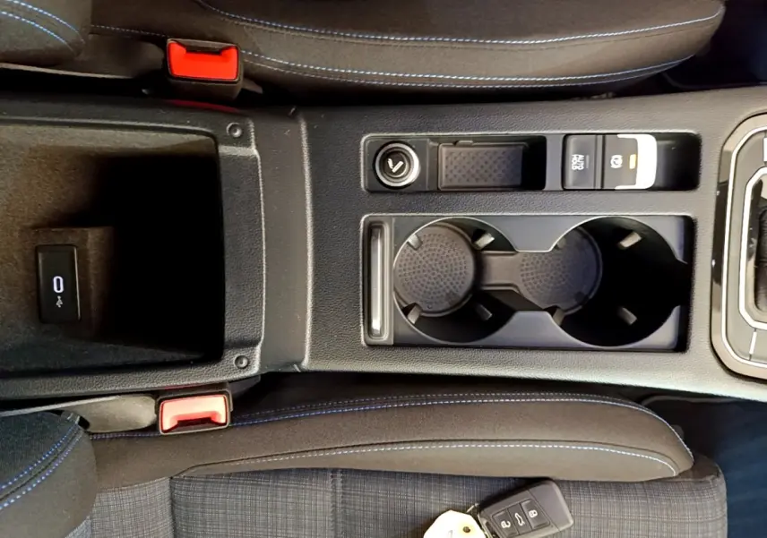 Vue plongeante sur la console centrale noire avec porte-gobelets et clé Volkswagen sur siège tissu gris à surpiqûres bleues.