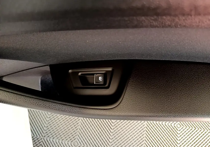 Gros plan sur le bouton d'ouverture électrique du coffre dans l'intérieur noir d'une Volkswagen Passat blanche.
