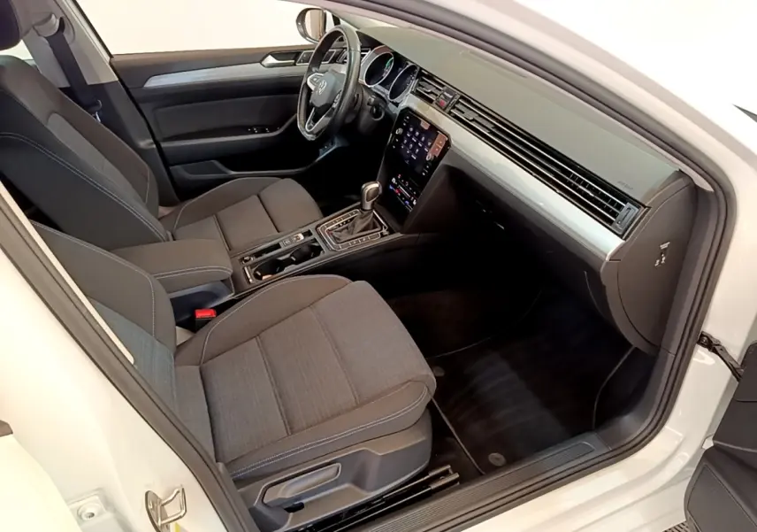 Intérieur avant droit de la Volkswagen Passat blanche, montrant sièges tissu gris et tableau de bord avec écran tactile.