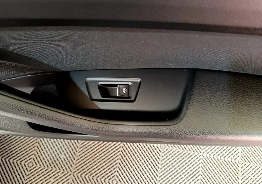 Gros plan sur le bouton d'ouverture électrique du coffre dans l'habitacle noir de la Volkswagen Passat hybride blanche.