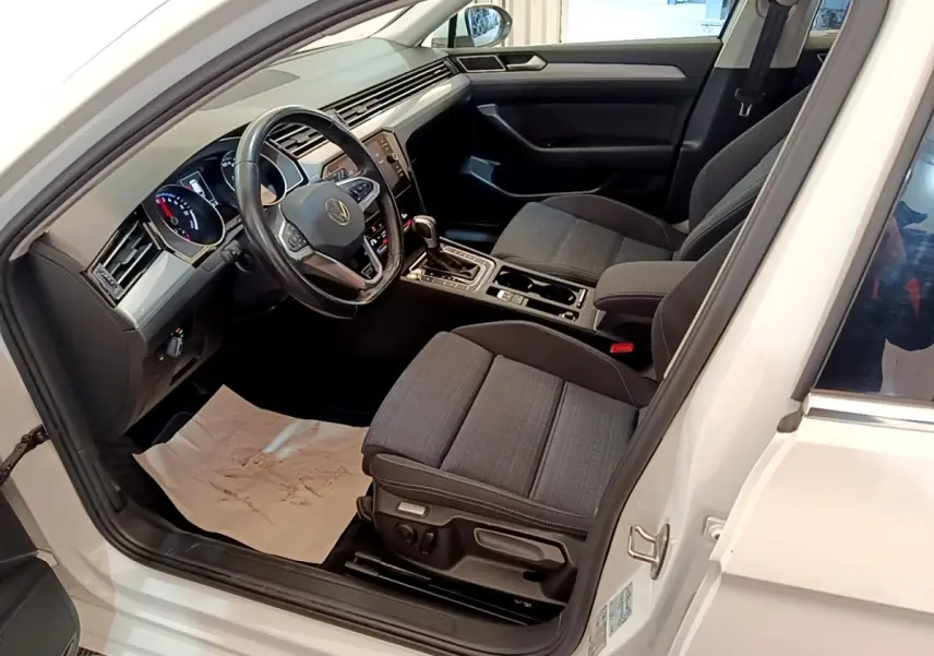 Vue intérieure côté conducteur d'une Volkswagen Passat blanche 2021, sièges tissu gris et tableau de bord digital.