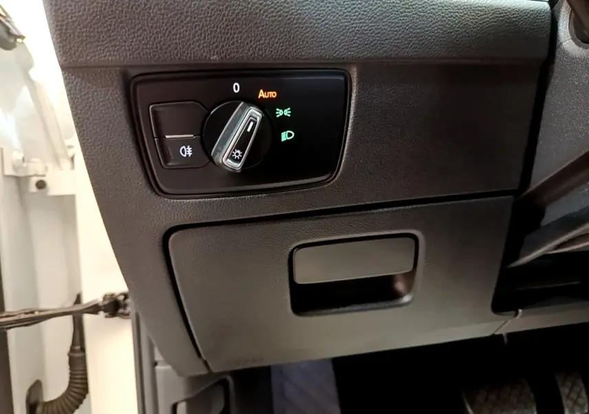 Détail du tableau de bord côté gauche avec commande des phares et partie de la portière blanche d'une Volkswagen Passat hybride.
