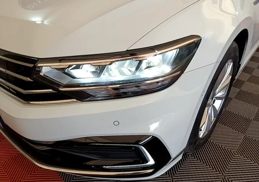 Gros plan sur l'avant droit blanc d'une Volkswagen Passat hybride avec phares LED allumés et jante visible.