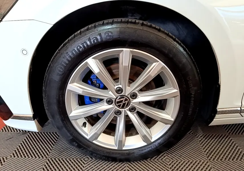 Gros plan sur la roue avant droite blanche d'une Volkswagen Passat hybride avec étrier de frein bleu visible.