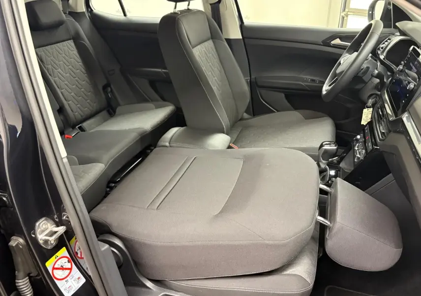 Intérieur du Volkswagen T-Cross noir intense 2024, vue côté gauche avec sièges avant rabattus et tableau de bord visible.