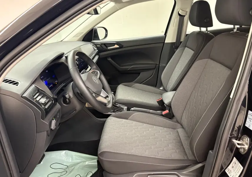 Vue intérieure côté conducteur du Volkswagen T-Cross 2024 noir intense, sièges tissu gris et tableau de bord moderne.