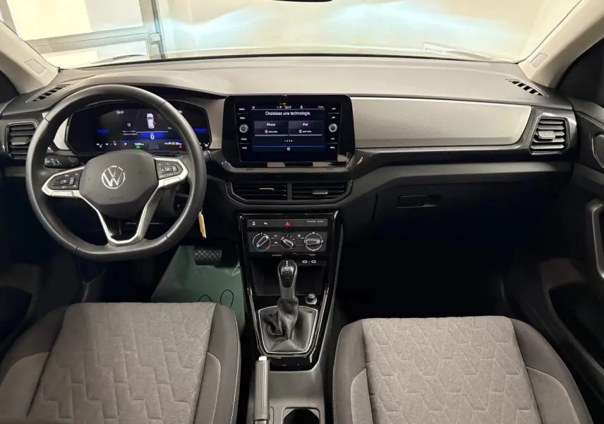 Vue intérieure frontale du tableau de bord et volant du Volkswagen T-Cross 2024 avec écran tactile et sièges gris.