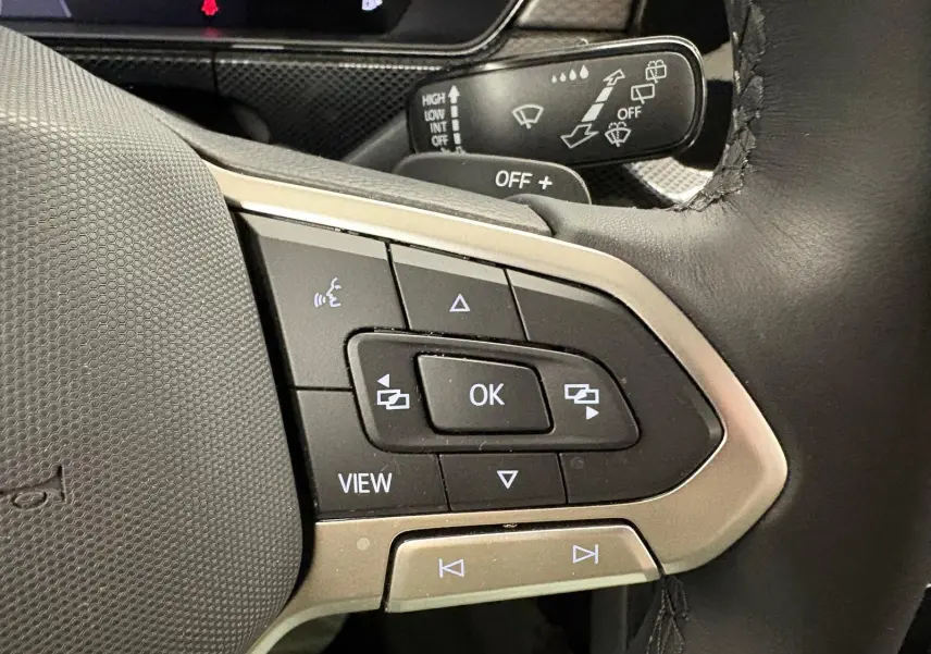 Gros plan sur les commandes au volant du Volkswagen T-Cross 2024 noir intense, avec boutons multifonctions et levier d'essuie-glace.