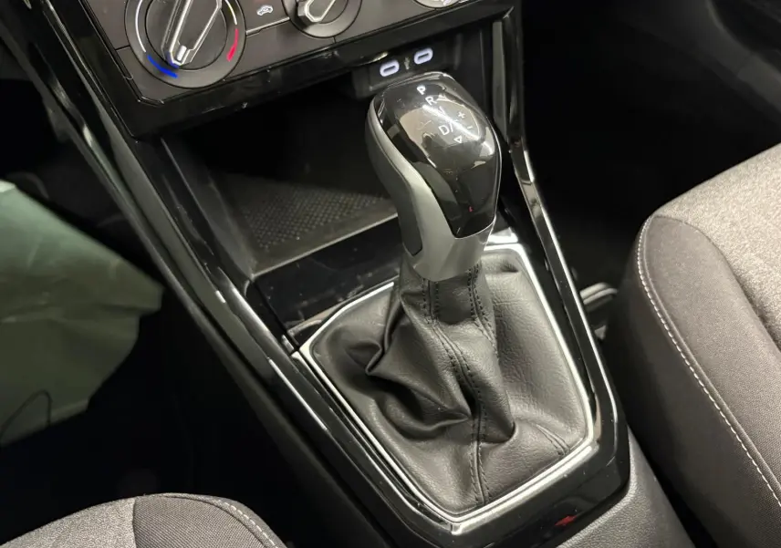 Le levier de vitesses automatique noir brillant du Volkswagen T-Cross 2024, avec console et sièges gris.