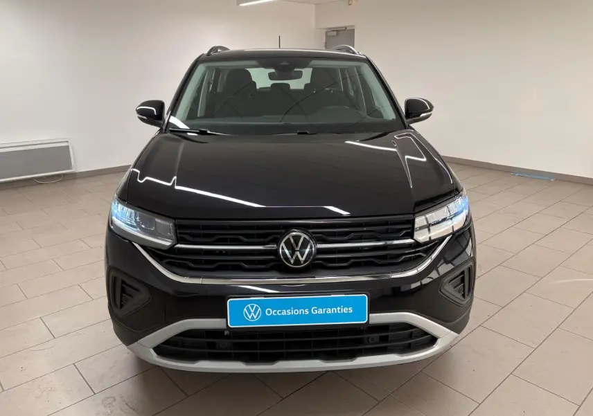 Vue frontale du Volkswagen T-Cross noir intense 2024 avec calandre chromée et phares LED allumés dans un showroom.