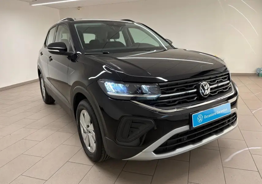 Volkswagen T-Cross noir intense en 3/4 avant droit, avec calandre chromée et phares LED allumés dans un showroom.