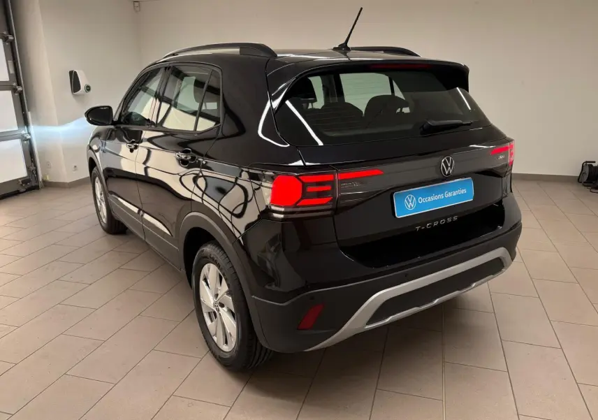 Volkswagen T-Cross noir intense vue 3/4 arrière droit en intérieur, avec feux arrière allumés et jantes argentées.