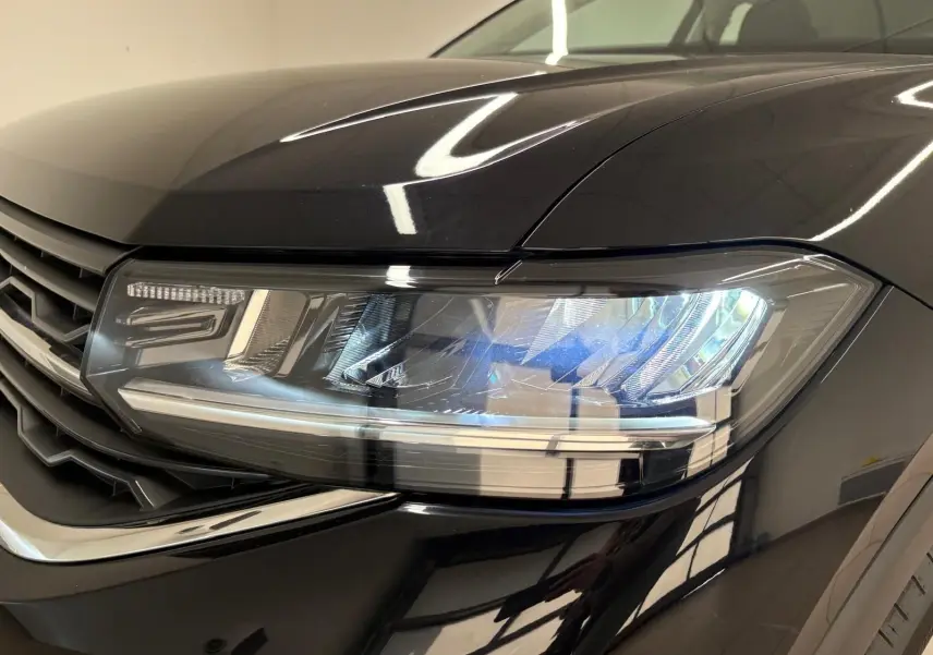 Gros plan sur le phare avant droit du Volkswagen T-Cross 2024 noir intense avec peinture métallisée brillante.
