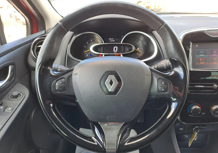 Vue centrée sur le volant noir brillant de la Renault Clio IV rouge, avec tableau de bord et écran tactile visibles.