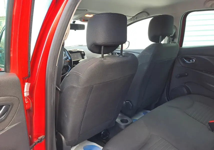 Vue intérieure arrière côté gauche de la Renault Clio IV rouge, montrant les sièges noirs et le tableau de bord à l'avant.