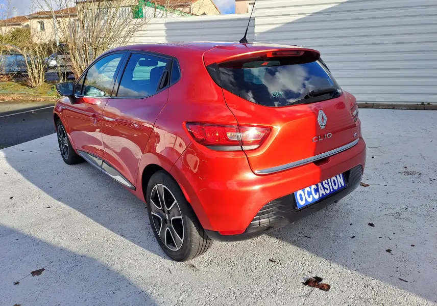 Vue 3/4 arrière droite d'une Renault Clio IV rouge 5 portes avec jantes alliage et plaque "OCCASION" visible.